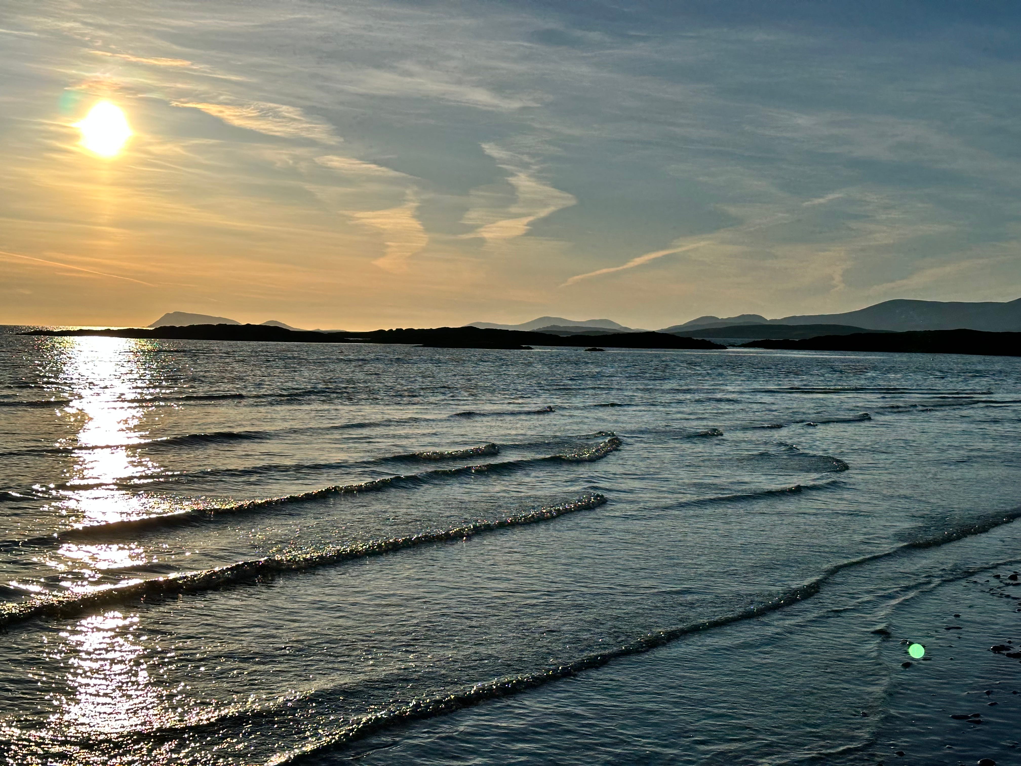 a setting sun glistening over little waves coming towards the photographer with silhouette of hills in the background